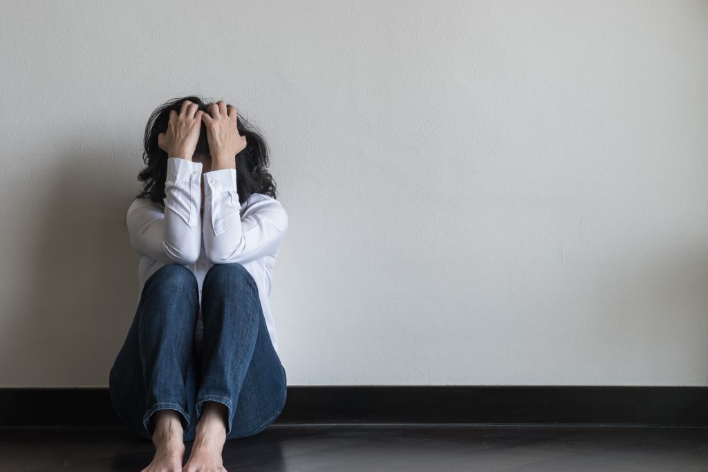 Stressed woman sitting on floor holding head.